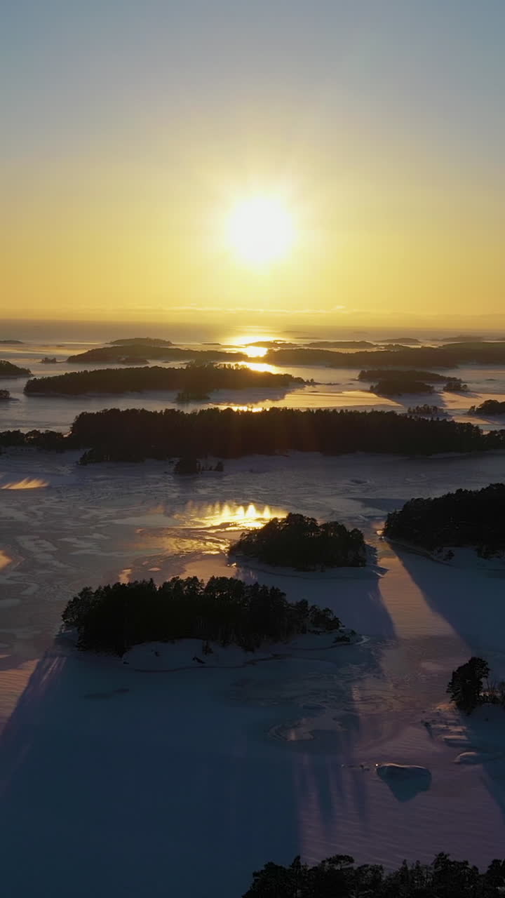 Vertical drone shot over islands in the Finnish archipelago, cold, winter sunset