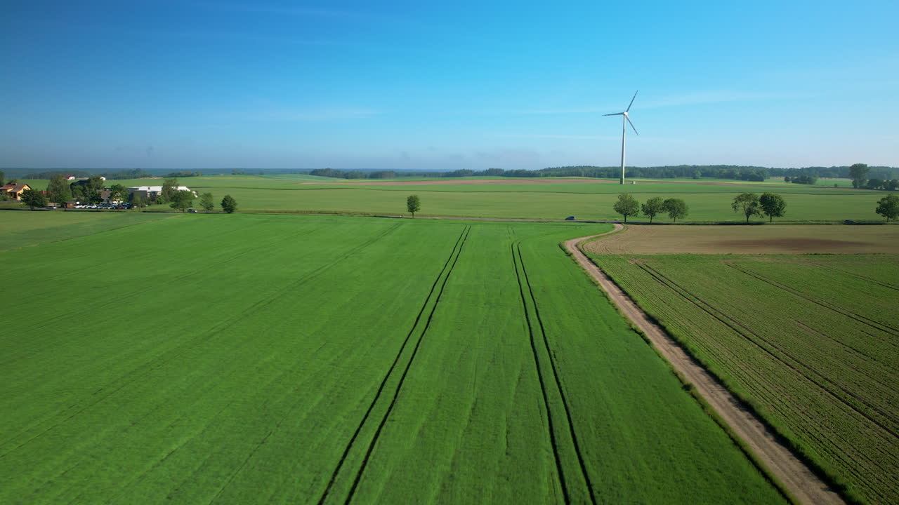 вид с воздуха, пересекающий сельскую местность в направлении вращающейся ветряной турбины на пышном сельскохозяйственном пастбище