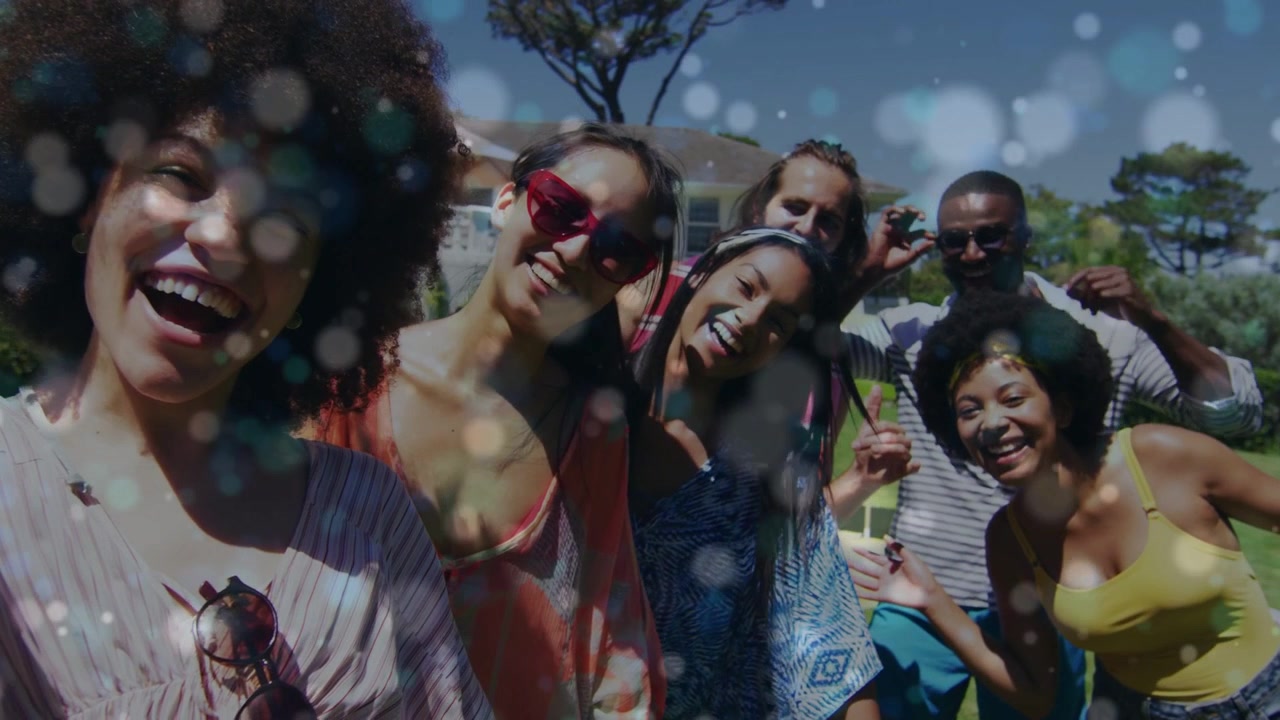 Portacellulare che riprende amici che si appoggiano e si aggiustano gli occhiali da sole in giardino, con effetto bokeh sovrapposto sull'obiettivo per i social.