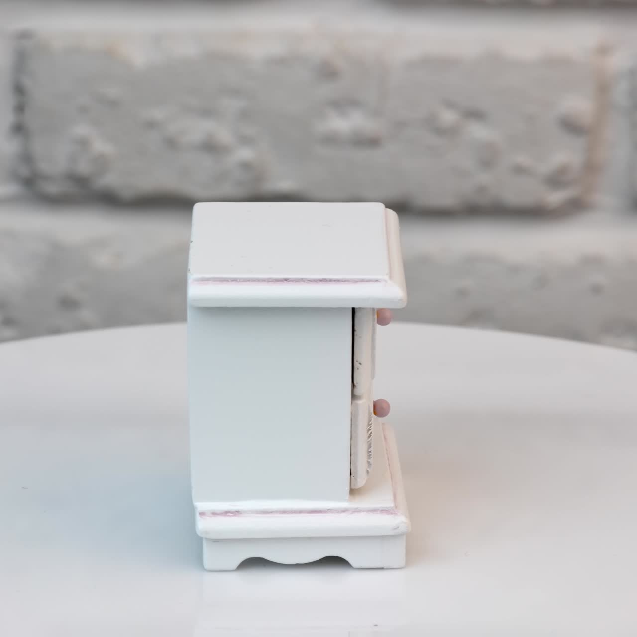 Cute little chest of drawers for doll's house. White wooden piece of interior rotating at the stand. Close up