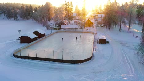 Gente-Jugando-2-Contra-2-Hockey-Sobre-Hielo-En-Arena-Rural-Durante-La-Puesta-De-Sol-Dorada,-Tiro-Aéreo-De-Drones