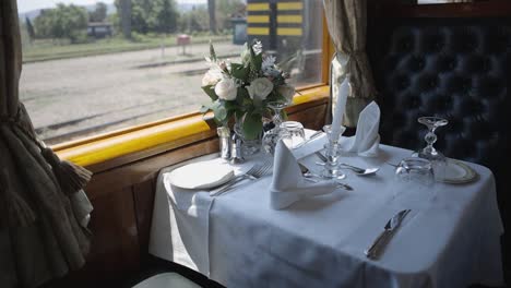 Dentro-De-Un-Vagón-De-Tren-De-Lujo,-Una-Elegante-Mesa-De-Comedor-Está-Elegantemente-Colocada-Y-Rezuma-Opulencia.