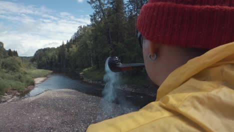 hombre fumando una pipa junto a un río en un bosque