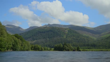 Weiße-Wolken,-Die-über-Berggipfeln-Aufsteigen,-Davor-Kiefernwälder,-Neben-Dem-Wasser-Des-Lake-Ennerdale,-Mit-Wolkenschatten,-Die-über-Die-Landschaft-Ziehen