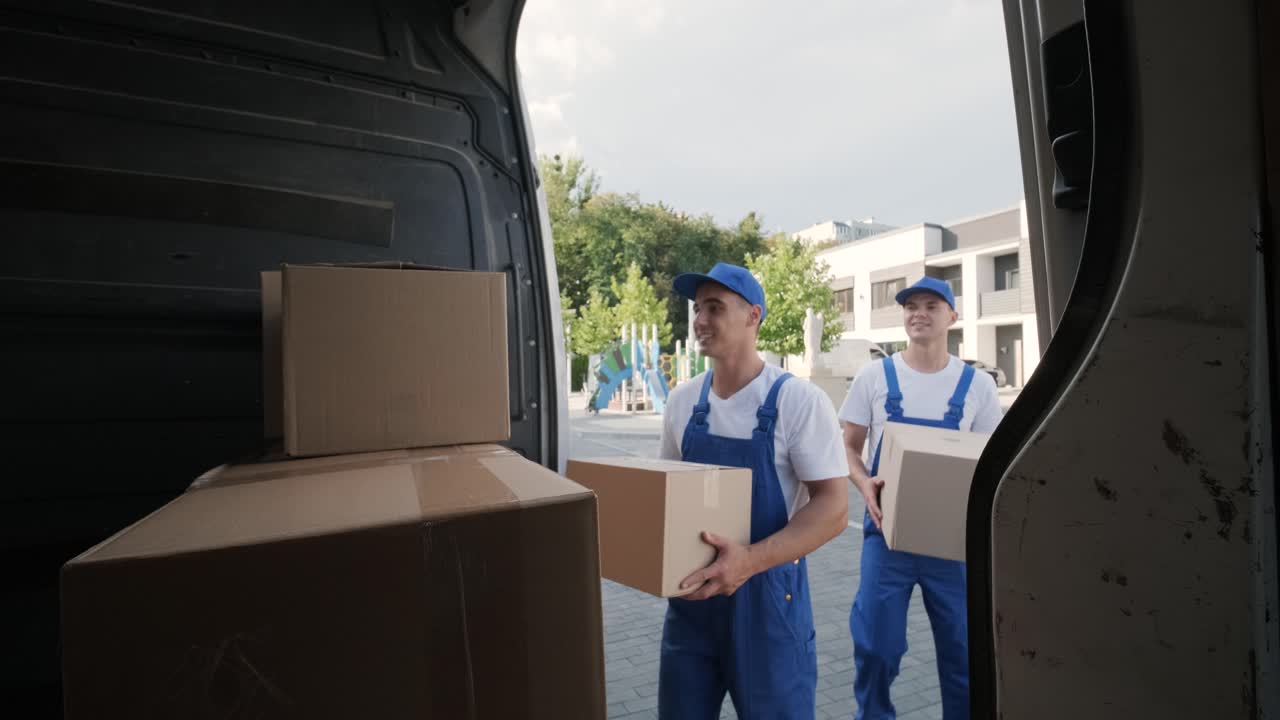 dos jóvenes trabajadores de una compañía de mudanzas están cargando cajas y muebles en un minibus
