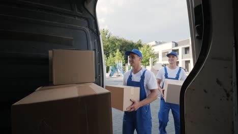 two young workers of removal company are loading boxes and furniture into a minibus