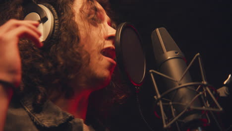 fotografía de cerca de un cantante masculino cantando una composición lírica en un micrófono en una habitación a prueba de sonido