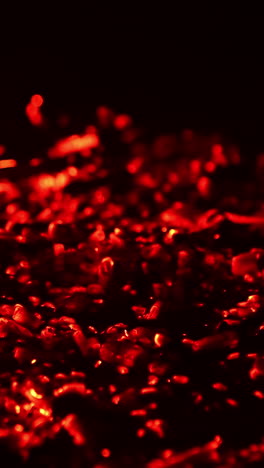 shimmering red light appearing in the smoldering embers. campfire burnt out and the hot pieces of charcoal flashing. close up. black backdrop. vertical video