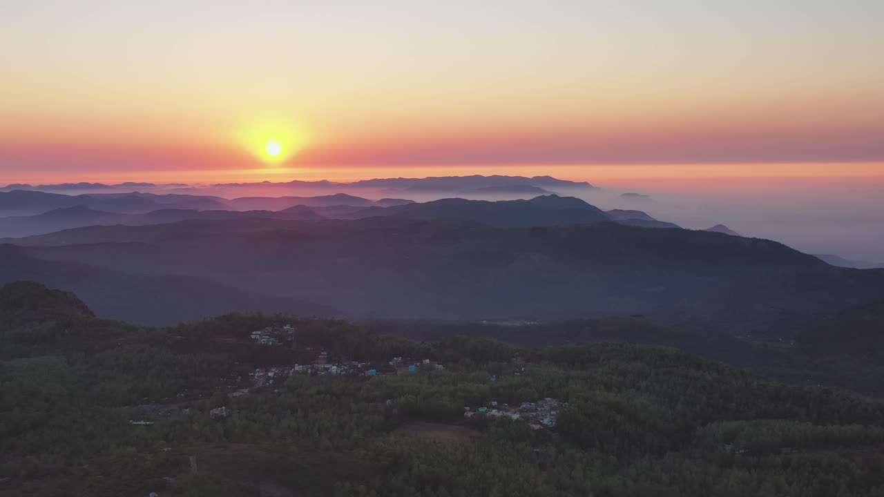 Las colinas boscosas de Yercaud emergen de la niebla matutina mientras el sol sale sobre las crestas montañosas en capas en Salem, Tamil Nadu, India. Una toma lenta de dron de gran angular captura el valle atmosférico y el pueblo de abajo.