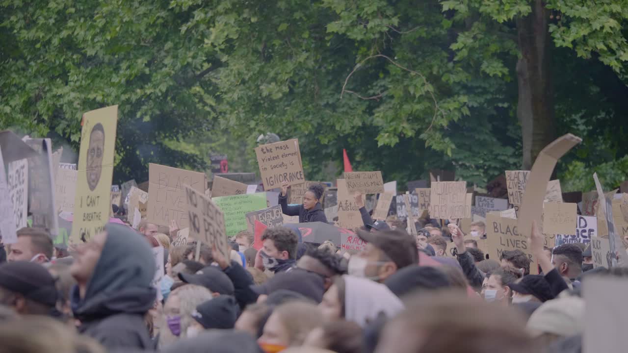 Big racially diverse crowd of protestors cheering and holding up signs against racism during a black lives matter protest in the rain in Stuttgart Germany.