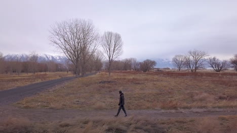 a man walks along a side trail towards a paved path - zoom out aerial