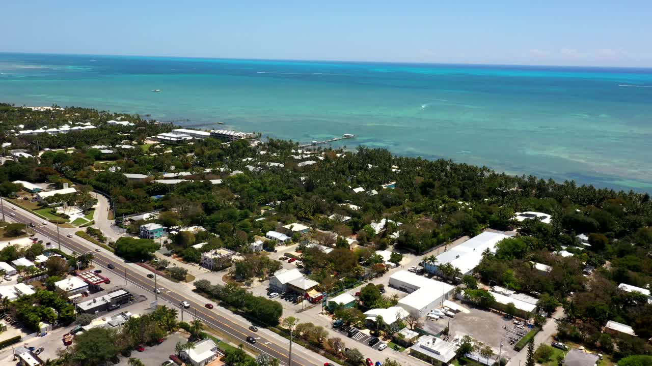 Aerial establishing orbit of town buildings surrounded by blue green ocean and palm trees