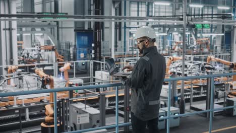 car factory engineer in work uniform using laptop computer. automotive industrial manufacturing facility working on vehicle production with robotic arms technology. automated assembly plant.