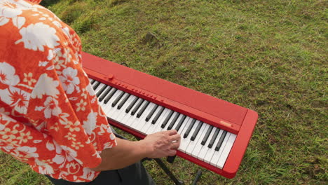 slow motion over the shoulder of a man playing the piano outside with green grass