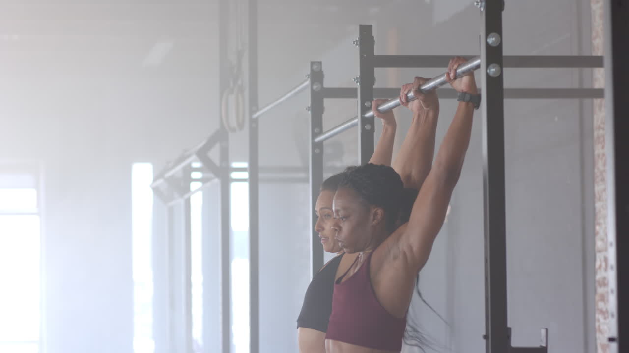 Doing pull-ups, two women exercising together in gym, focusing on fitness goals, copy space