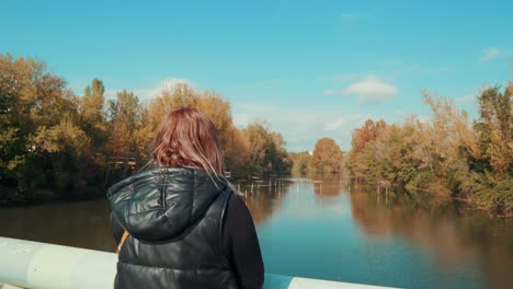 Ein-Mädchen,-Das-Am-Frühen-Morgen-Auf-Der-Brücke-Steht-Und-Mitten-Im-Wald-Auf-Den-Fluss-Blickt,-Montpellier,-Frankreich