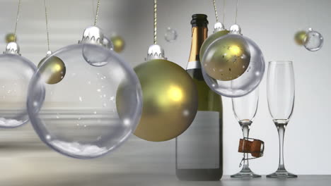 swinging gold and clear christmas baubles over champagen bottle and glasses on grey background