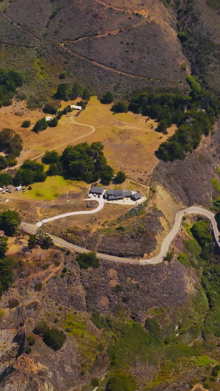 Stunning view of mountainous landscape of the ocean shore at Morro Bay, California, USA. Few houses and winding highway on the rocky coastline from aerial view. Vertical video