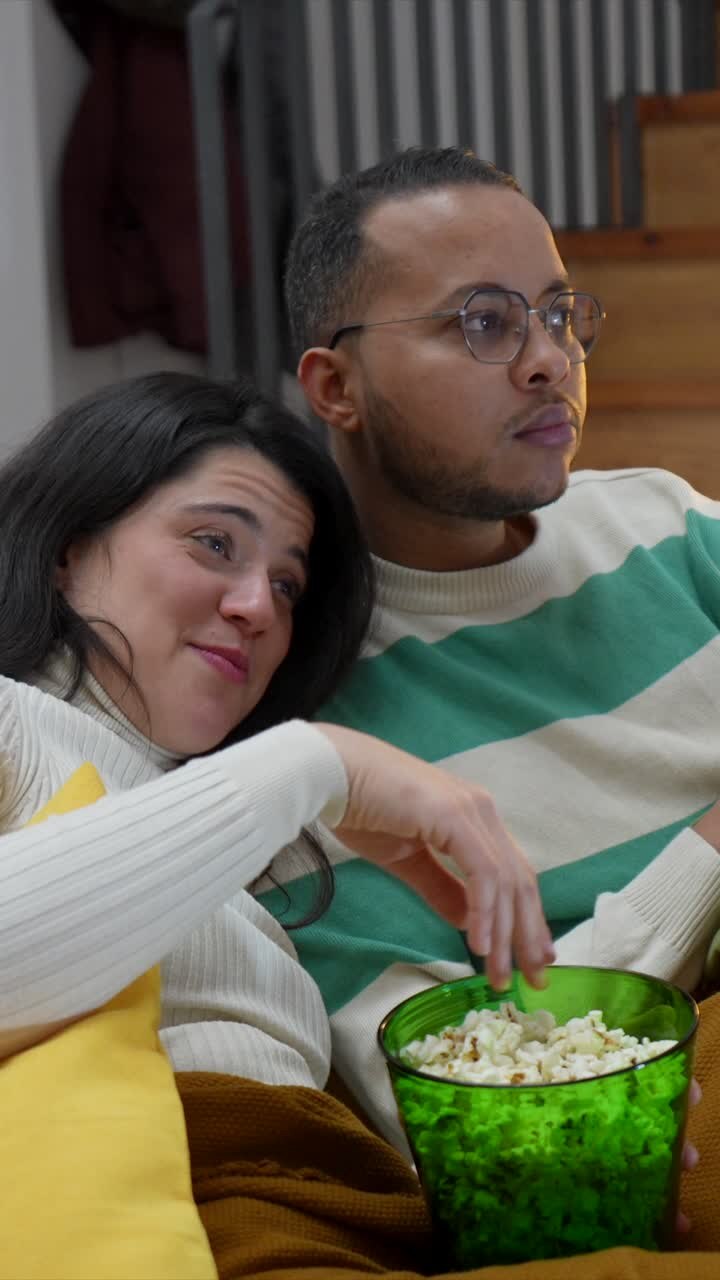 Coppia felice che guarda la TV e mangia popcorn sul divano