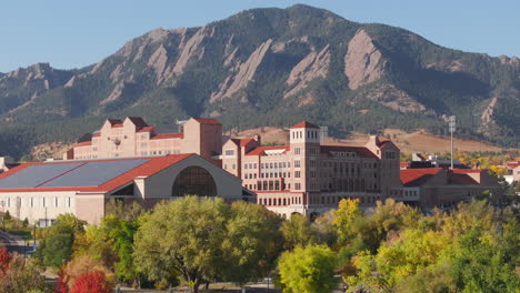 vista aérea de cerca del campus y el estadio de cuu boulder rodeado de árboles de otoño verdes y amarillos con las montañas rocosas flatiron en el fondo en la cordillera delantera de colorado