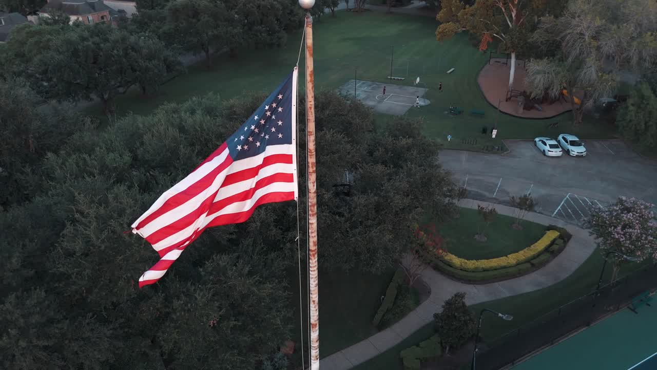 An aerial view of an American flag flowing in the air, on a pole, in slow motion