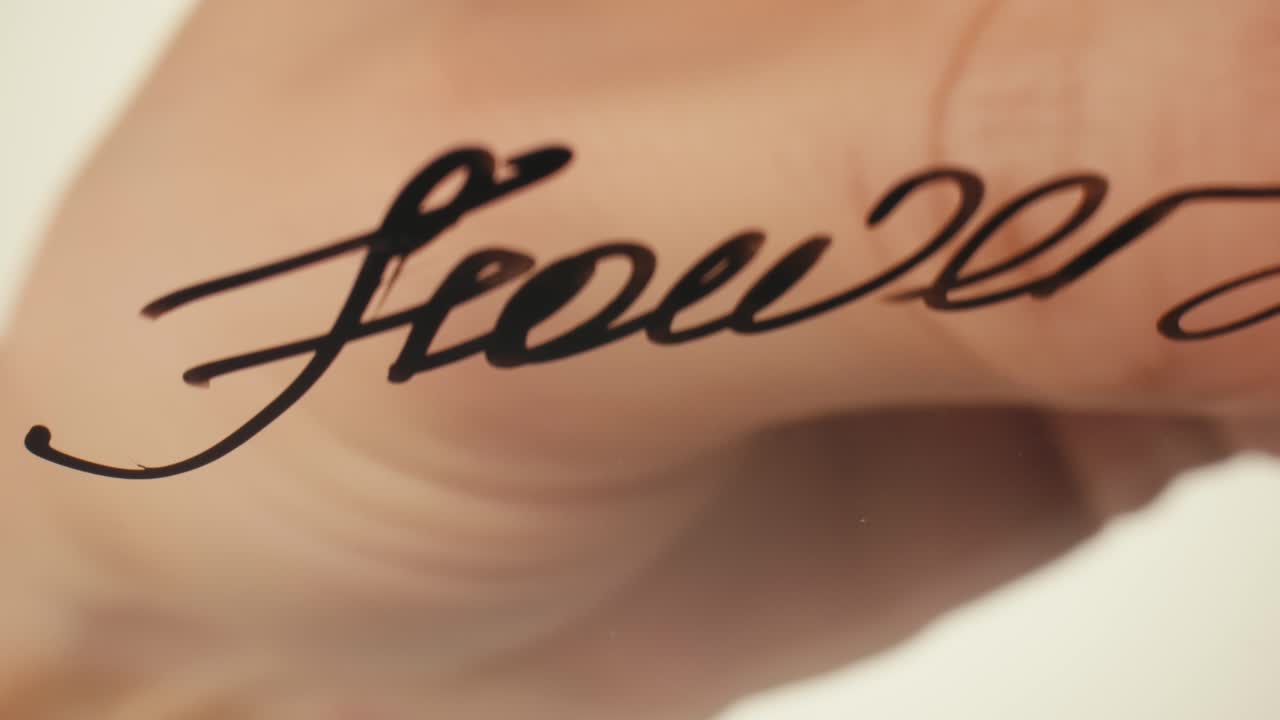 Close-Up of Hand Writing 'Flower' on Glass Surface