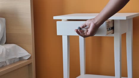 person opening a drawer of a white nightstand in a bedroom