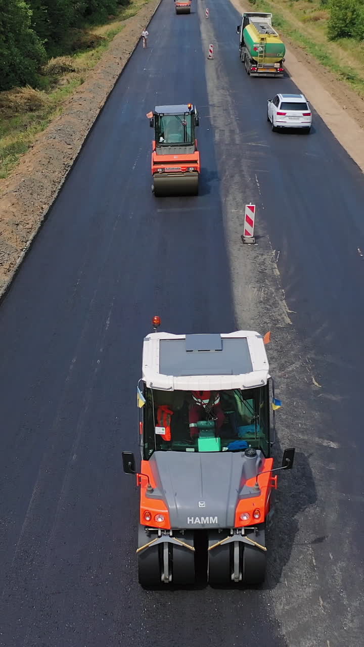 Repairing with vibration roller. Aerial view of the new asphalt road under construction Vertical video