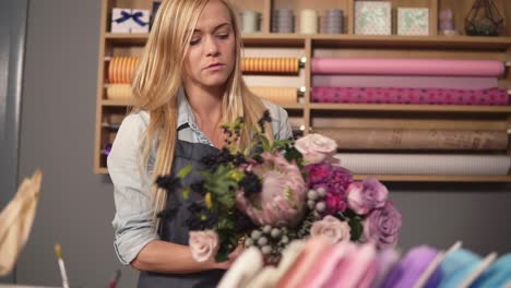 Young-female-florist-making-a-modern-bouquet-of-flowers.-She-is-putting-flowers-on-the-table.-Slow-Motion-shot