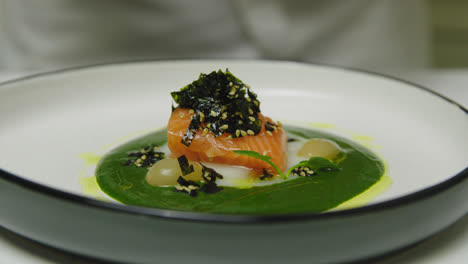 close up shot of professional chef in luxury restaurant adding greens on fancy served salmon plate