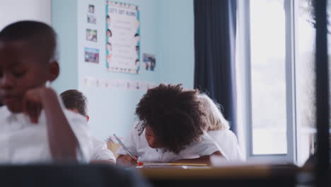 group of elementary school pupils wearing uniform working at desks raise hands to answer question