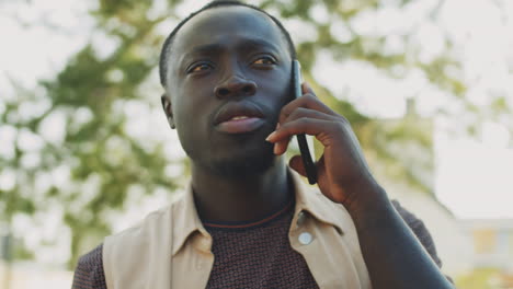 Black-Man-Standing-Outdoors-with-Coffee-and-Speaking-on-Phone