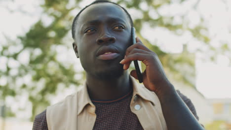 hombre negro de pie al aire libre con café y hablando por teléfono