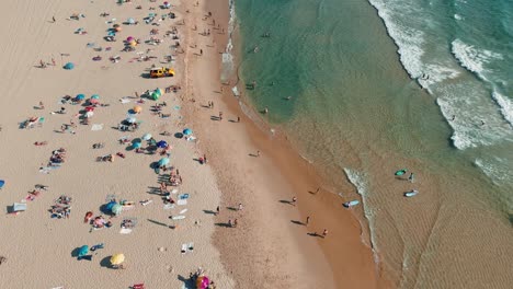 Aerial view of a crowded beach with people, umbrellas, and surfboards
