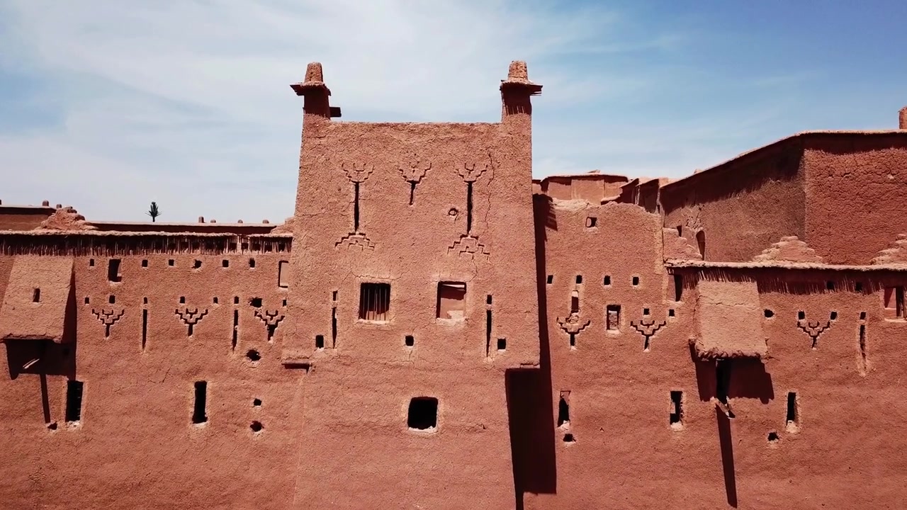 Vue de face d'un mur de kasbah symétrique à Ait Benhaddou, Maroc, orné de symboles berbères traditionnels et d'une surface en pisé texturée. Forte composition géométrique idéale pour les projets culturels, architecturaux et