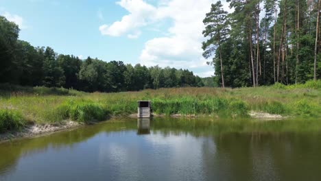 "Drone-glides-over-Europe's-dawn-lit-lake,-capturing-tranquil-lagoon,-lush-forest,-and-natural-ponds