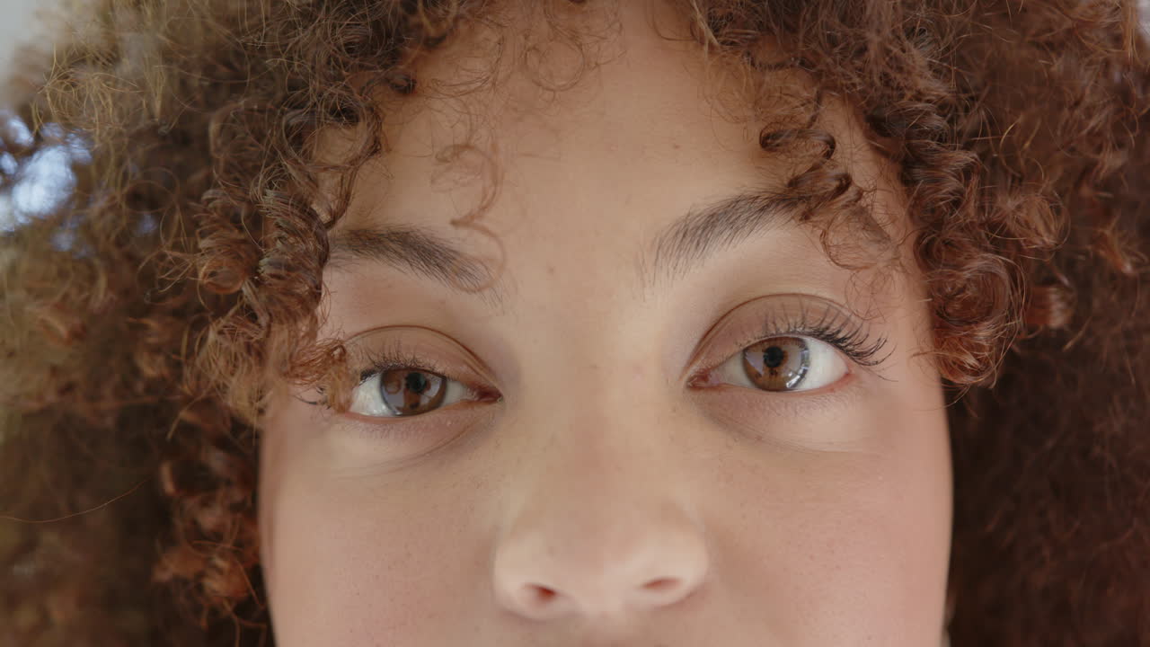 Close-up of woman with curly hair, smiling and touching her face