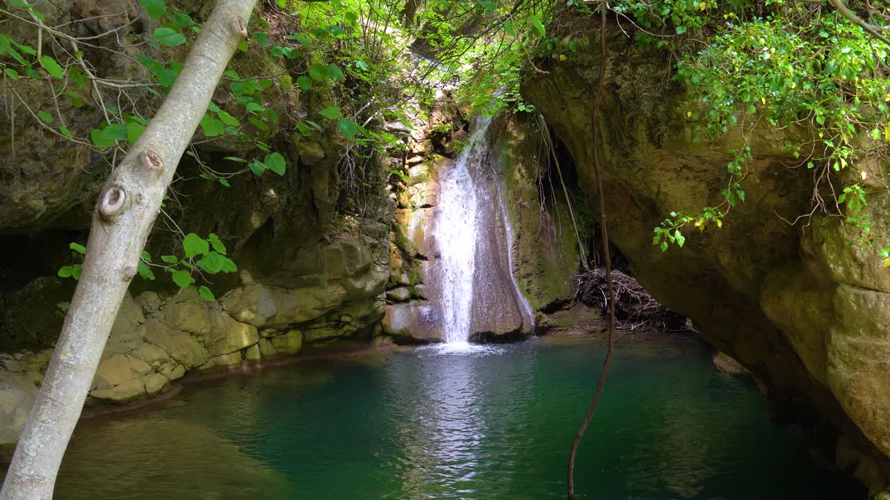Luce solare che illumina la cascata di Kefalogourna, circondata da vegetazione verde e rocce muschiose, isola di Thassos, Grecia