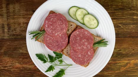 abrir sándwiches de salami con pan, pepino, perejil en una placa blanca girar lentamente.