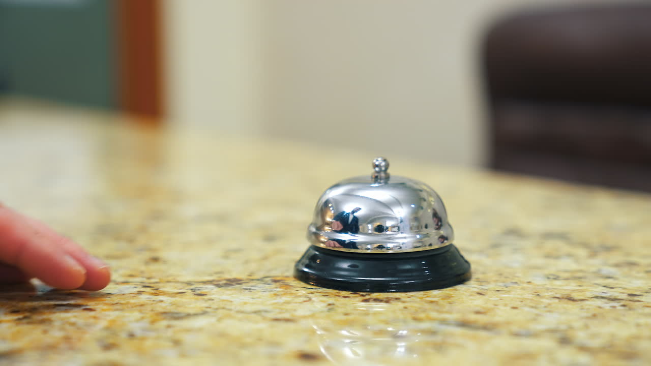 Hotel bell on reception table. Man's hand presses bell button to call the receptionist in the hotel. Customer touches the metal alarm. Close-up.