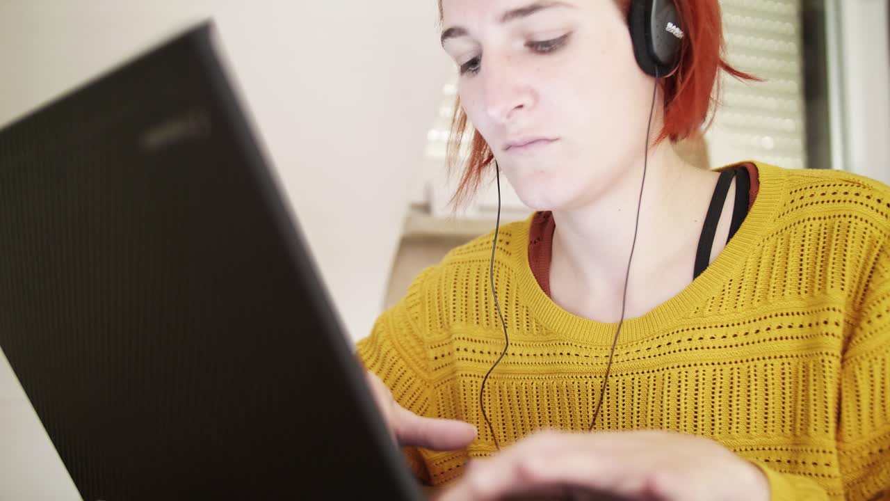 una joven pelirroja con auriculares está escribiendo en una laptop en casa