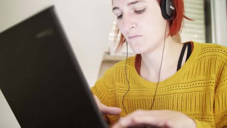 A-Young-red-haired-girl-with-headphones-is-typing-on-a-Laptop-at-Home