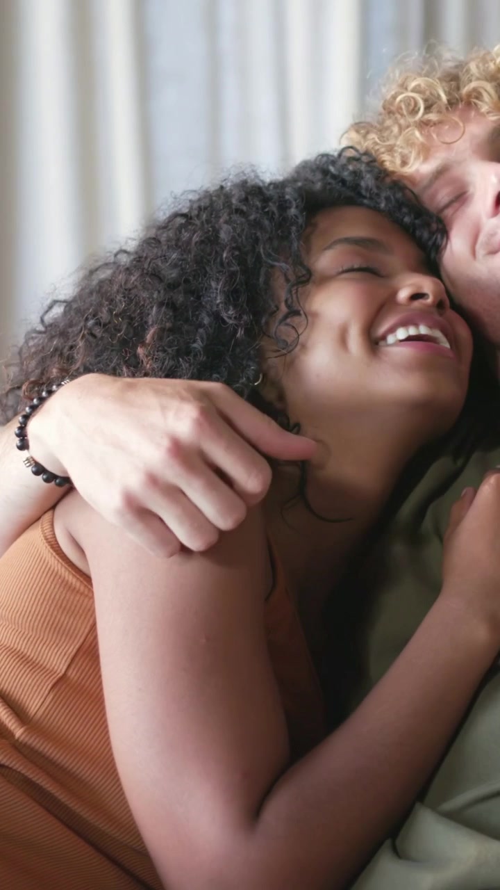 Vertical video: Smiling woman in tank top nestling on partner's lap after laugh at home, wristwatch
