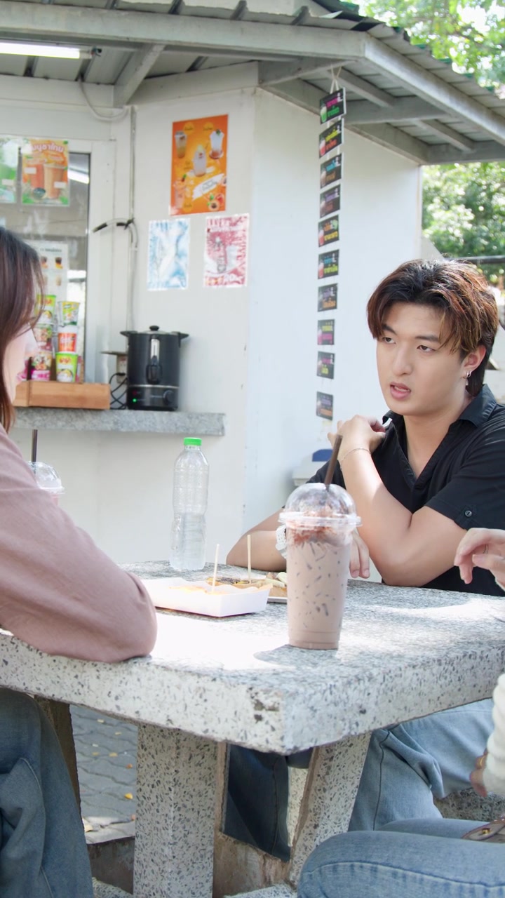 นักเรียนชาวเอเชียวัยหนุ่มสาวนั่งอยู่ที่โต๊ะหิน กินอาหารริมทางและดื่มสมูทตี้กลางแจ้ง