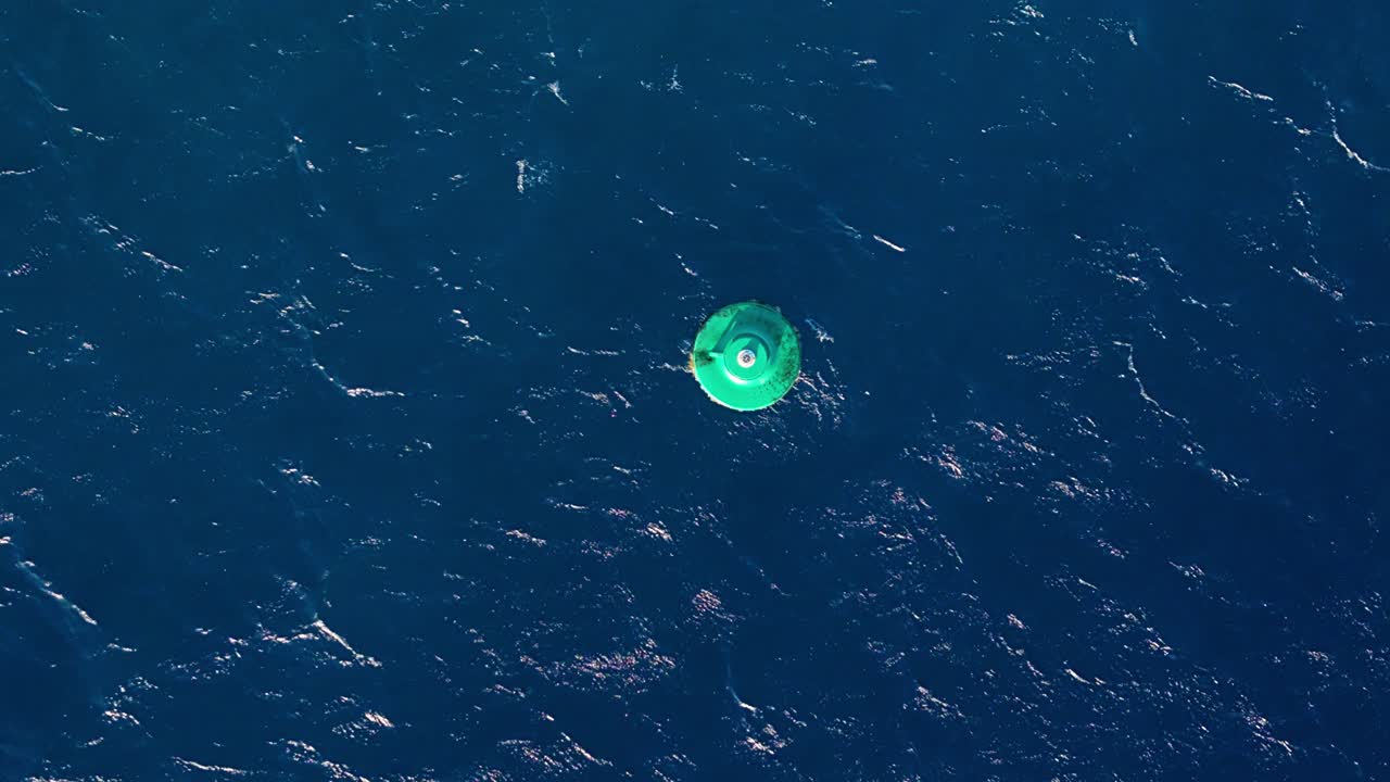 드론에서 위상으로 내려온 대형 녹색 내비게이션 보이가 열린 바다 물에서 흔들리고 있습니다.