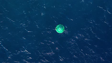 drone top down satellite view of large green navigation buoy bobbing in open ocean water