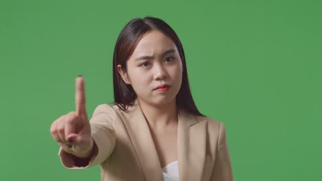 close up of asian business woman showing stop, one finger gesture, taboo sign, standing on green screen in the studio