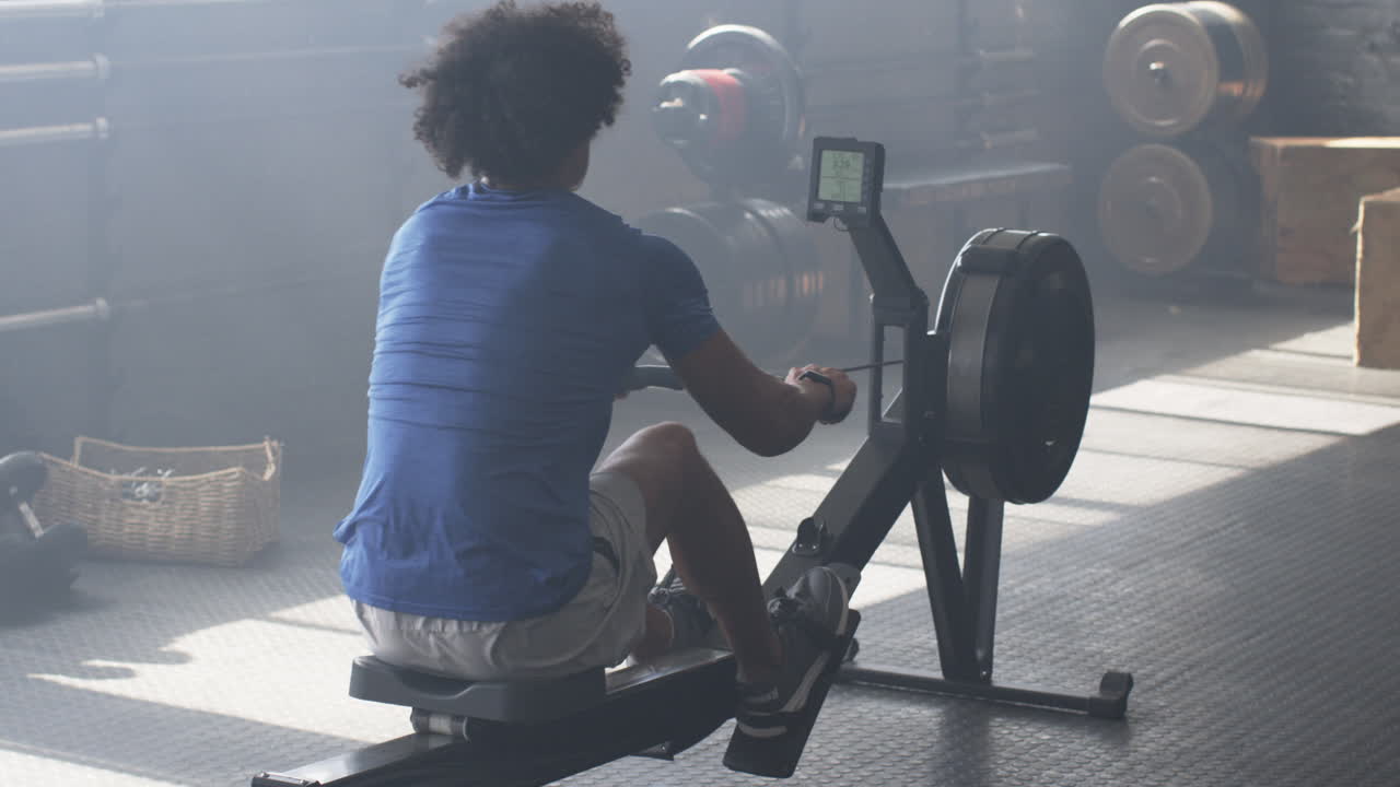 Using rowing machine, man exercising in gym, focusing on fitness goals