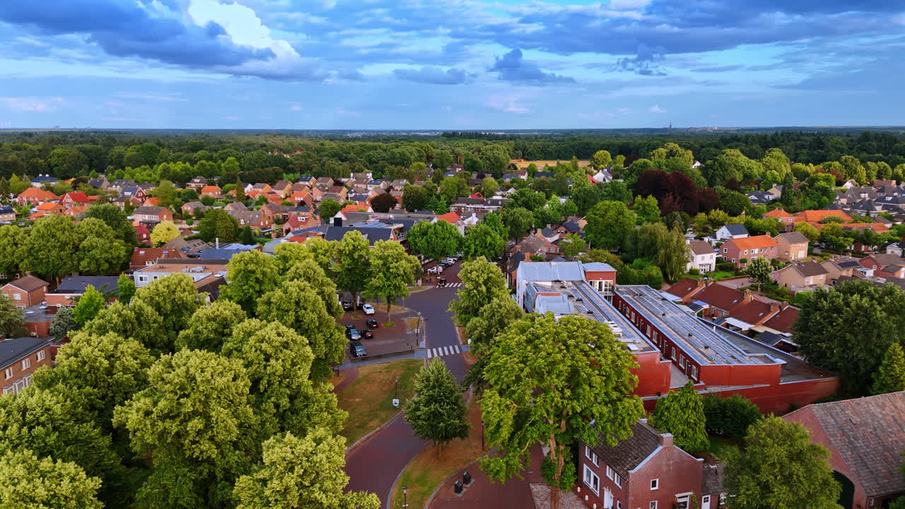 Flygvy över bostadsgata med tät grönska. Drönarbild av förortshus omgivna av täta gröna träd och trädgårdar under en mjuk blå himmel