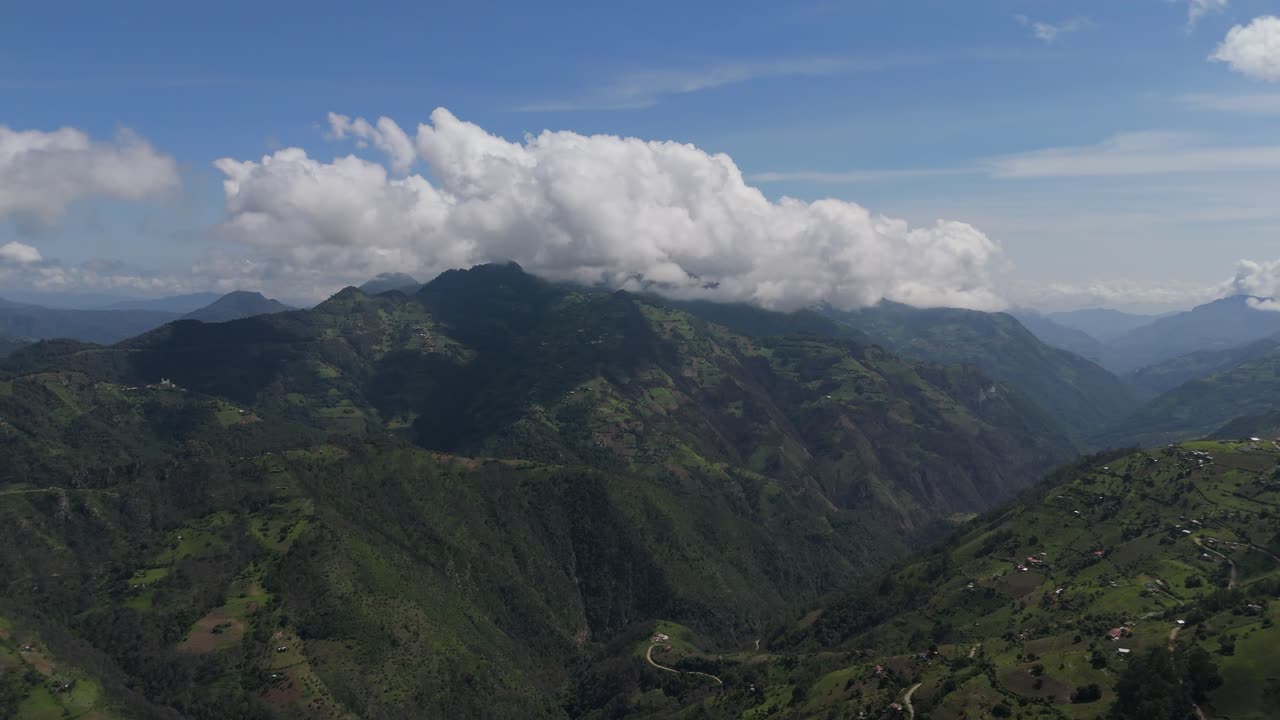 Soft clouds float above lush green mountains in this stunning aerial landscape view.